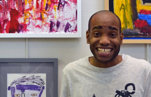 Man smiling in front of framed art pieces.